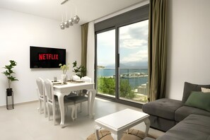 A modern living room with a dining area, a flat-screen TV mounted on the wall, and a large window offering a view of the sea. - Apartment 'Sea View Uno 2' with Sea View, Wi-Fi and Air Conditioning (Agios Nikolaos)