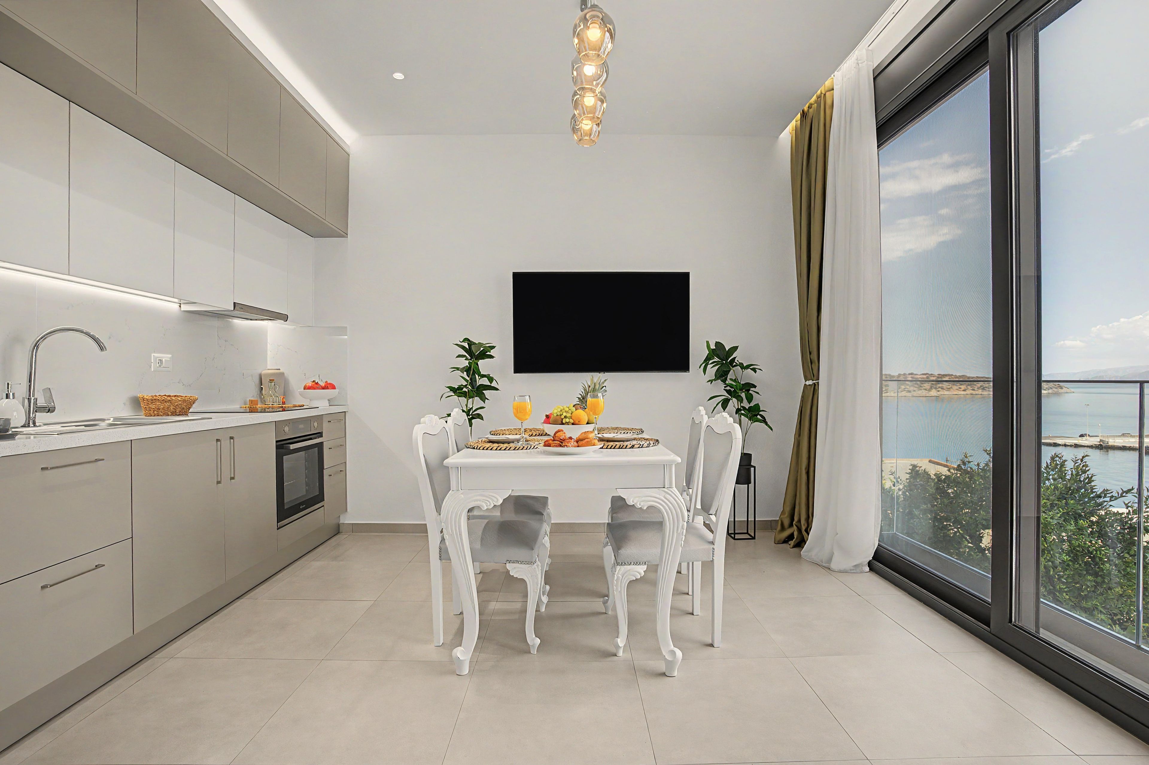 A modern kitchen with a dining area, a flat-screen TV, and a large window with a view.