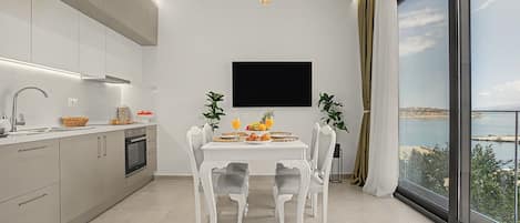 A modern kitchen with a dining area, a flat-screen TV, and a large window with a view.