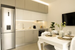 A modern kitchen with a built-in refrigerator, a dining table set for four, and a flat-screen TV mounted on the wall. - Apartment 'Sea View Uno 2' with Sea View, Wi-Fi and Air Conditioning (Agios Nikolaos)