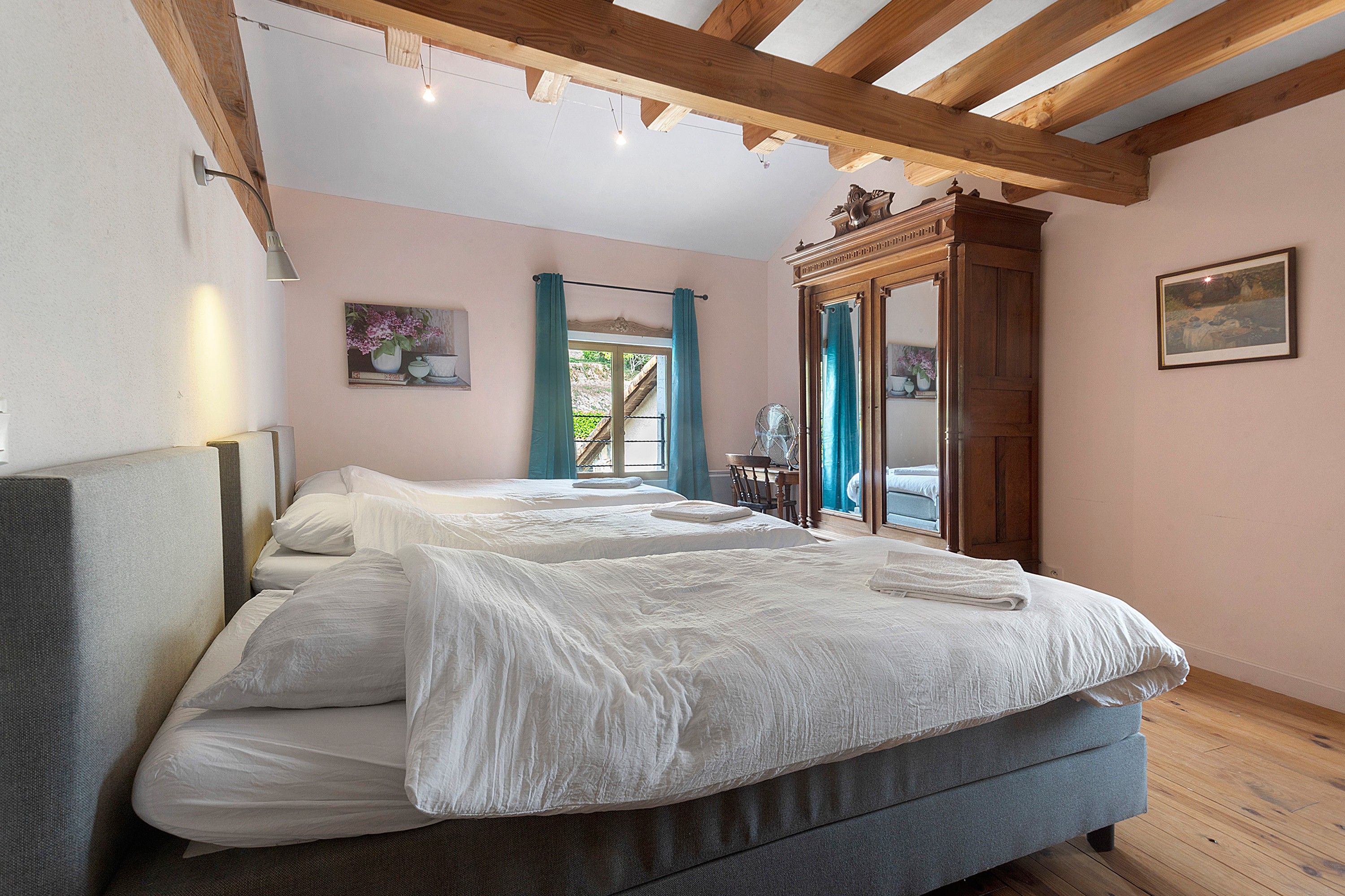 Une chambre avec un grand lit, un plafond en bois, une fenêtre avec des rideaux et un miroir.
