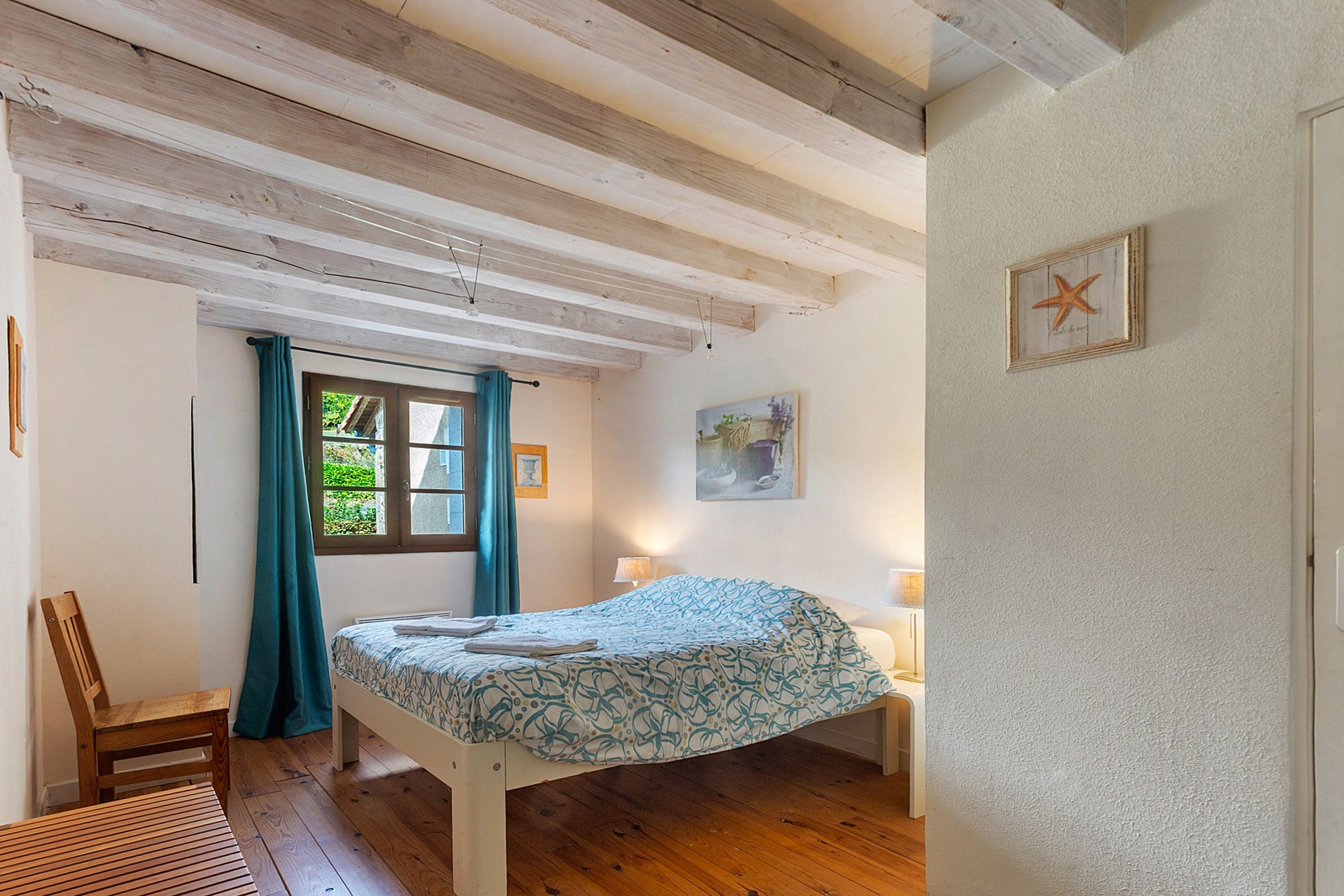 Quarto com cama, cadeira, janela com cortinas, luminária e quadro na parede.