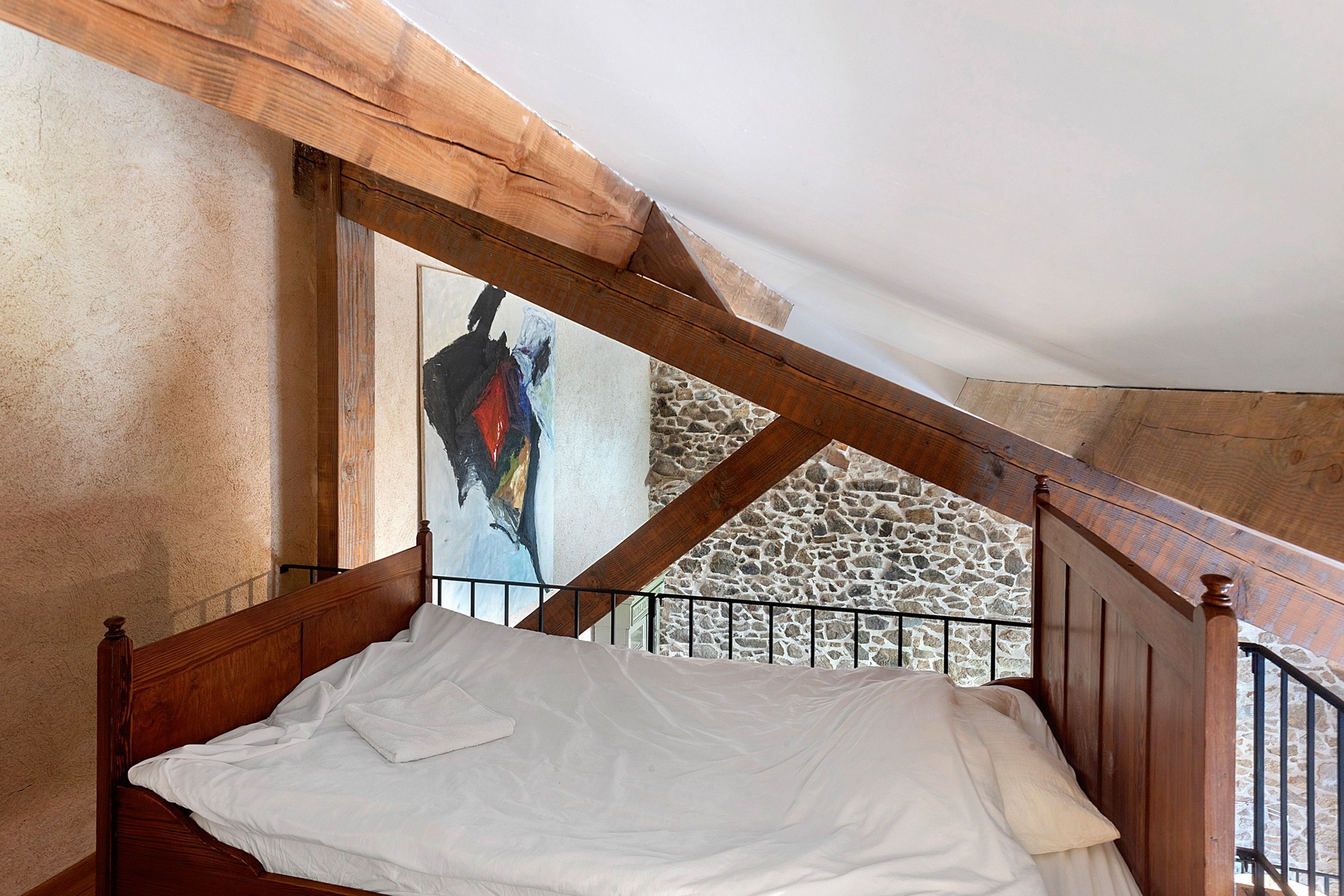 Ein Schlafzimmer mit einem hölzernen Bett, einer Steinsäule und einem Gemälde.
