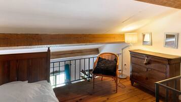 Una habitación con piso de madera, una cama, una silla, un aparador y un balcón con baranda.