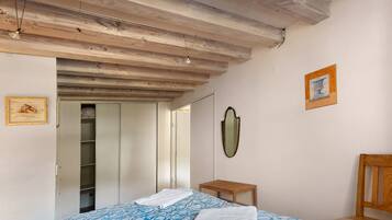 Quarto com cama, cadeira de madeira, mesa de cabeceira, espelho e porta que dá para outro cômodo.