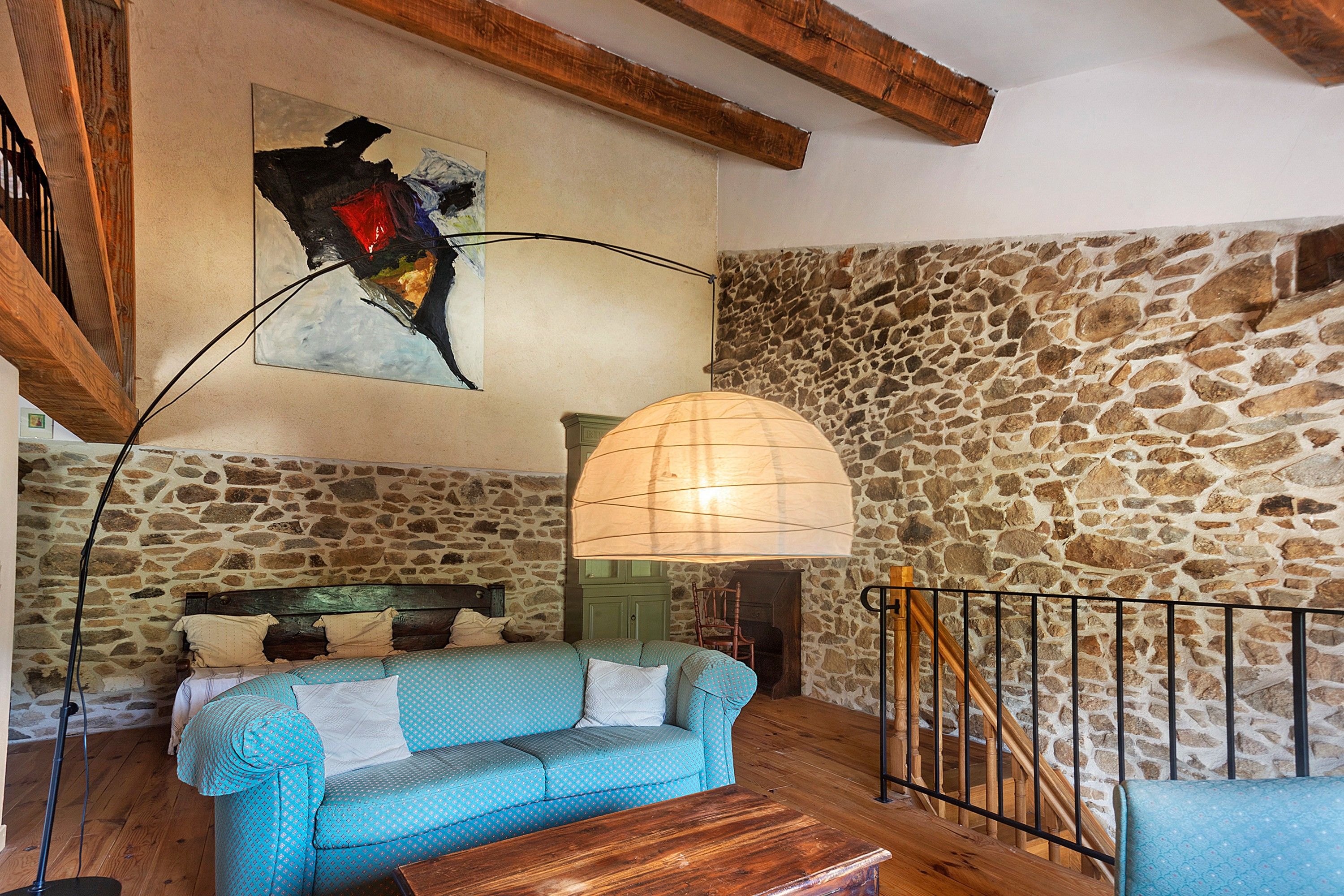 Ein gemütliches Zimmer mit Steinwand, Holzboden und einer blauen Couch, einer Stehlampe und einem Gemälde.