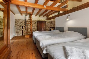 Ein Schlafzimmer mit zwei Betten, Holzbalken, einer Steinwand, einem Holzschrank und einer Leitern.
