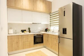 Eine moderne Küche mit Holzschränken, einem eingebauten Backofen, einem Edelstahlkühlschrank und einem Fenster mit Jalousien.