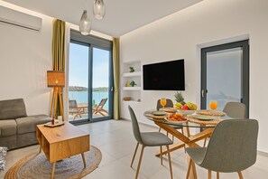 A modern living room with a glass table, grey chairs, a sofa, and a TV mounted on the wall. - Apartment 'Sea View Uno 1' with Sea View, Wi-Fi and Air Conditioning (Agios Nikolaos)