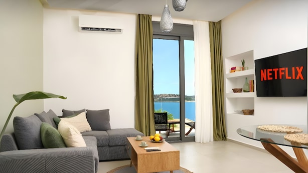 A modern living room with a grey sofa, a wooden coffee table, and a view of the sea through a large window. - Apartment 'Sea View Uno  1' with Sea View, Wi-Fi and Air Conditioning (Agios Nikolaos)