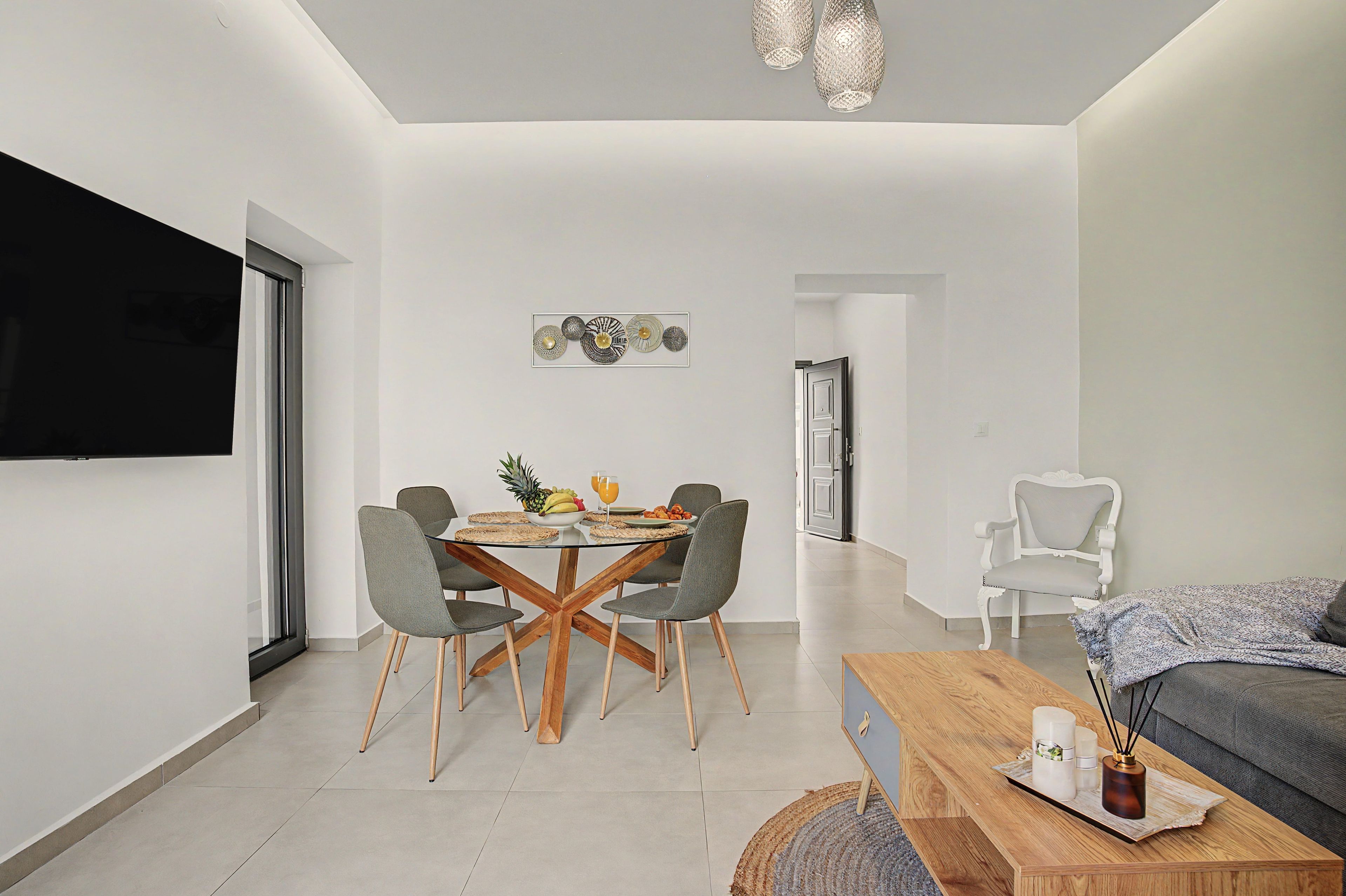 A modern living room with a dining area, a flat-screen TV mounted on the wall, and a cozy seating area with a sofa and a coffee table.