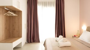 A modern hotel room with a wooden wardrobe, a bed with white linens, and a bedside table with a bottle and books. - Apartment 'Sea View Uno  1' with Sea View, Wi-Fi and Air Conditioning (Agios Nikolaos)