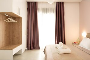 Ein modernes Hotelzimmer mit einem Holzschrank, einem Bett mit weißer Bettwäsche und einem Nachttisch mit einer Flasche und Büchern.