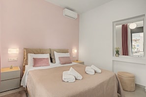 A hotel room with a bed, bedside tables, a window with curtains, and a view of the outside. - Apartment 'Sea View Uno 1' with Sea View, Wi-Fi and Air Conditioning (Agios Nikolaos)
