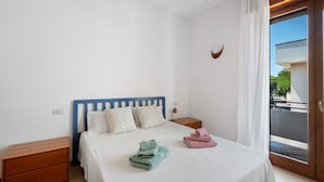 Ein Schlafzimmer mit einem Bett, zwei Nachttischen, einem Fenster mit Vorhängen und Blick ins Freie.