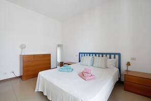 A hotel room with a bed, a wooden dresser, a nightstand, and a lamp.