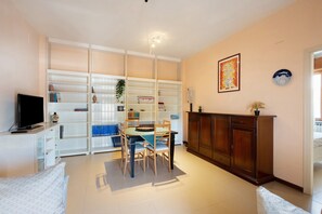 A living room with a television, a dining table with chairs, a bookshelf, and a cabinet.