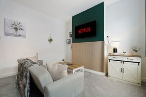 Ein Wohnzimmer mit einer Couch, einem Couchtisch, einem an einer grünen Wand befestigten Fernseher und einem Schrank mit Holzeinlage.