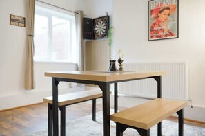 Een kamer met een houten tafel en bank, een dartbord, een poster en een radiator.