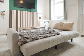 Ein modernes Wohnzimmer mit einer Couch, einem Fernseher, einem Schreibtisch und einem Fenster.