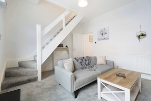 Ein Wohnzimmer mit grauem Sofa, Couchtisch, Treppe und Heizkörper.