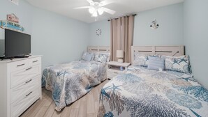 A bedroom with two beds, a ceiling fan, a TV on a dresser, and a clock on the wall. - Gulf-view condo steps from the beach Regatta 102a (Gulf Shores)