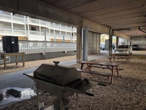 An outdoor covered parking area with picnic tables, a barbecue grill, and a pool in the background. - Gulf-view condo steps from the beach Regatta 102a (Gulf Shores)