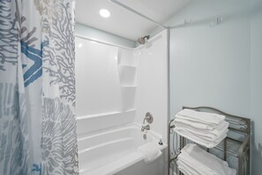 A bathroom with a bathtub, a shower, and a towel rack with folded towels. - Gulf-view condo steps from the beach Regatta 102a (Gulf Shores)