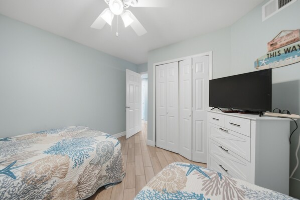 A bedroom with two beds, a ceiling fan, a television on a dresser, and a door leading to another room. - Gulf-view condo steps from the beach Regatta 102a (Gulf Shores)