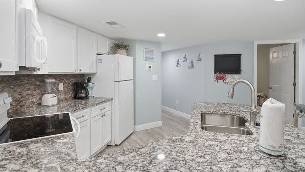 A modern kitchen with white cabinets, granite countertops, a built-in refrigerator, and a stainless steel sink. - Gulf-view condo steps from the beach Regatta 102a (Gulf Shores)