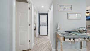 A hallway with a white door, a laundry area with a washing machine, and a table with nautical decorations. - Gulf-view condo steps from the beach Regatta 102a (Gulf Shores)