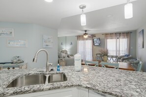 A kitchen with a granite countertop, stainless steel sink, and a ceiling fan. - Gulf-view condo steps from the beach Regatta 102a (Gulf Shores)