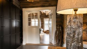 A hallway with a wooden floor, a rustic lamp, and a door leading to a room with a bed.