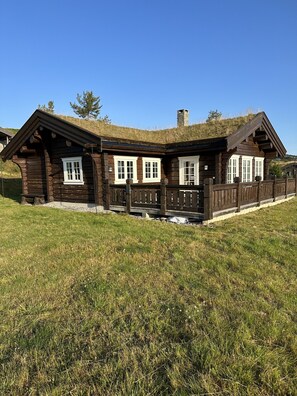 Eine Blockhütte mit einem Steinkamin, Fenstern mit weißem Rahmen und einem Holzzaun.