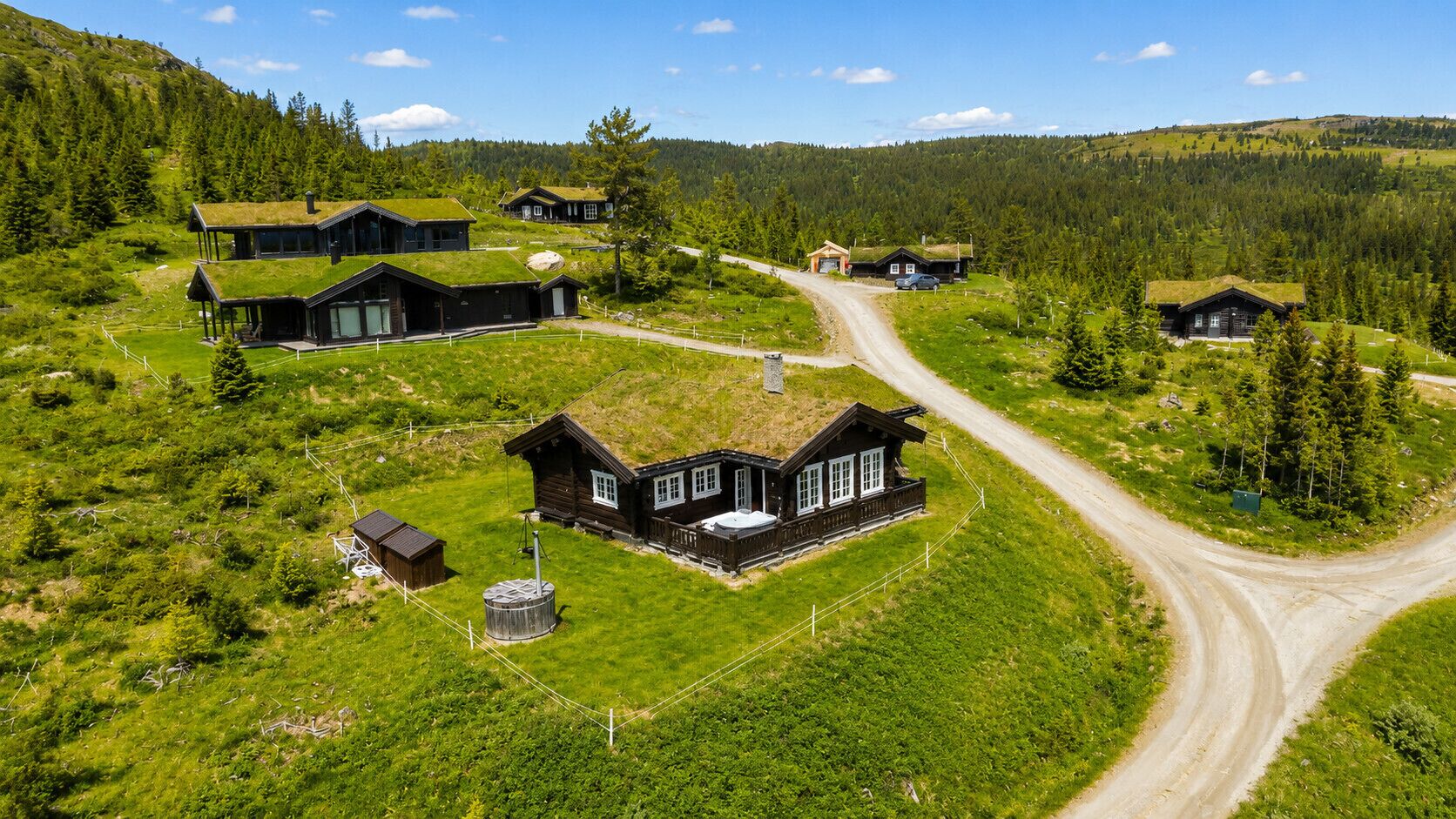 Een afgelegen, groen landschap met verschillende houten hutten, een onverharde weg en een heldere lucht.