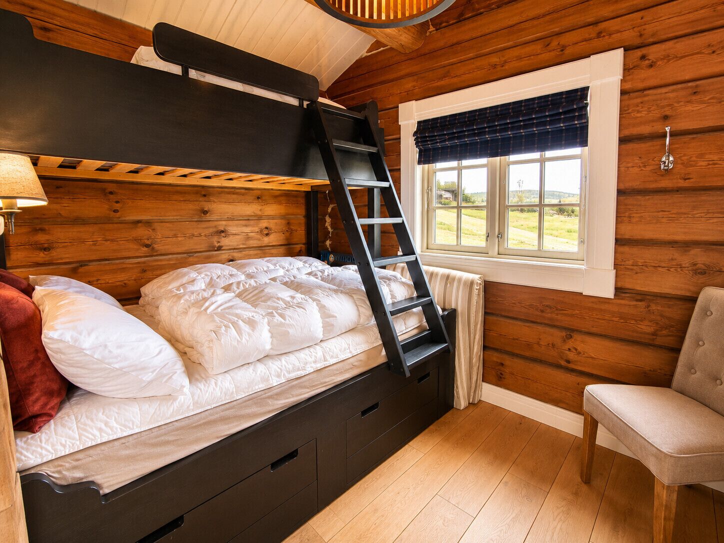 A bunk bed with a ladder, a window with a view, a chair, and a lamp.