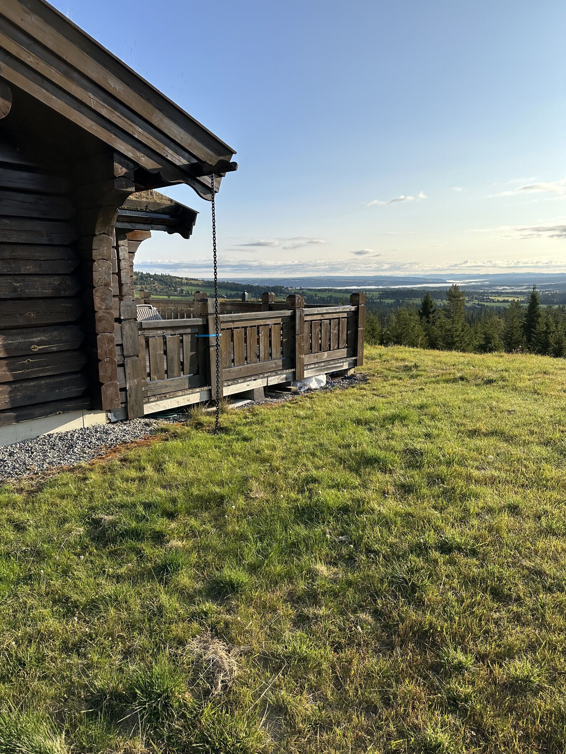 Een houten chalet met veranda, uitkijkend over een grasveld en het verre landschap.