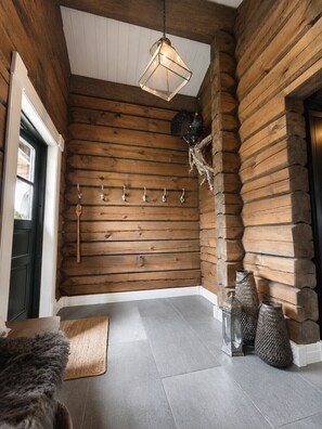 Ein Holzblockhaus-Interieur mit einer Holzwand, einer hängenden Lampenleuchte, einem Kleiderständer und einer Tür.