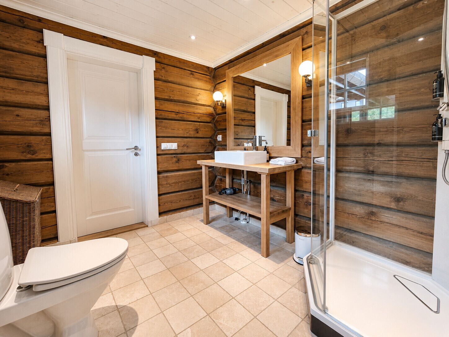 A bathroom with a wooden interior, a white toilet, a sink with a mirror, and a glass-enclosed shower.