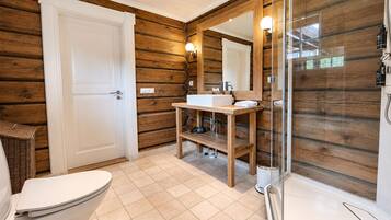A bathroom with a wooden interior, a white toilet, a sink with a mirror, and a glass-enclosed shower.