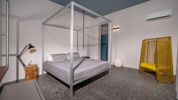 Ein modernes Schlafzimmer mit einem Himmelbett, einer Nachttischlampe, einem kleinen Holfnachtkästchen, einem gelben Sessel und einer weißen, kugelförmigen Dekoration am Boden.