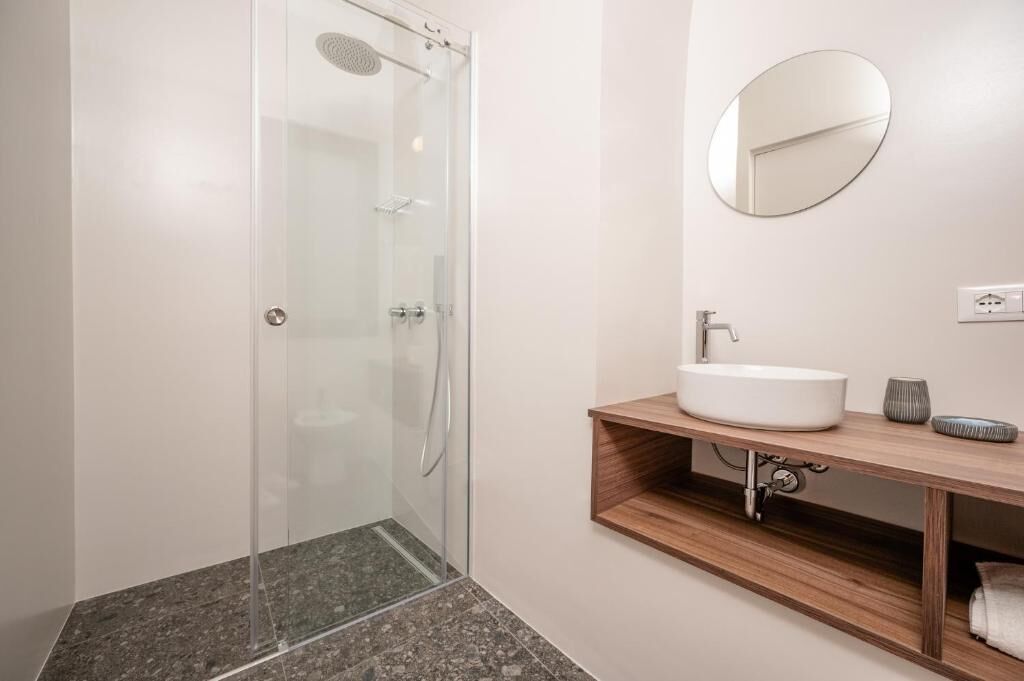 Ein modernes Badezimmer mit einer Duschkabine aus Glas, einem Holzlagerfläschchen und einem runden Spiegel.