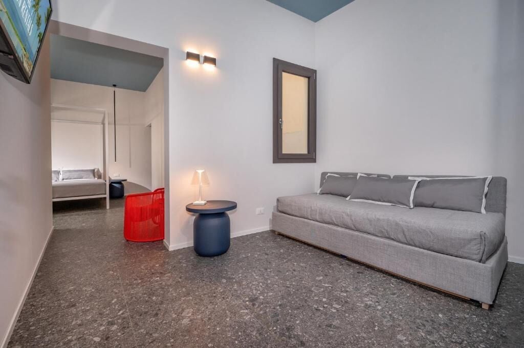 A modern living room with a grey sofa, a red basket, a blue side table, and a wall-mounted mirror.