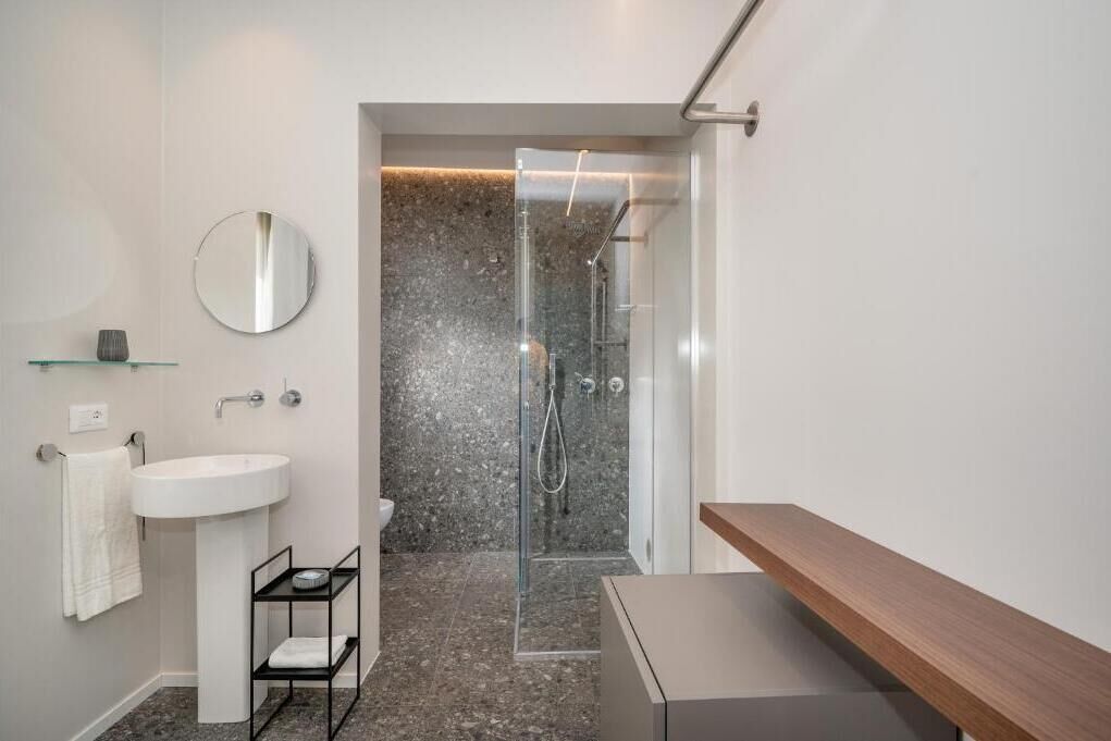 Un bagno moderno con doccia vetrata, lavabo bianco e mobile contenitore in legno.