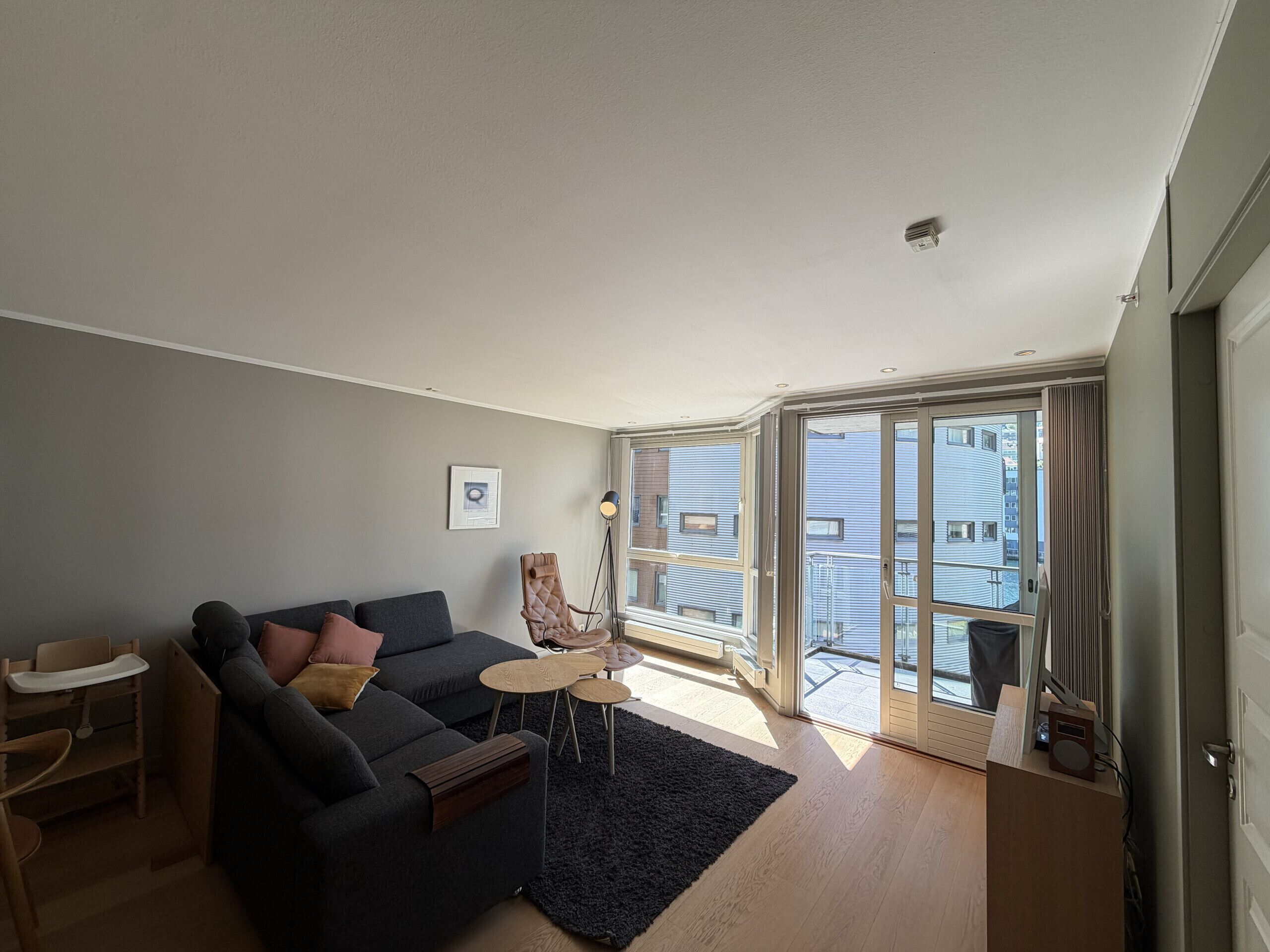 A modern living room with a sofa, a small table, a chair, and a view through a glass door to the outside.