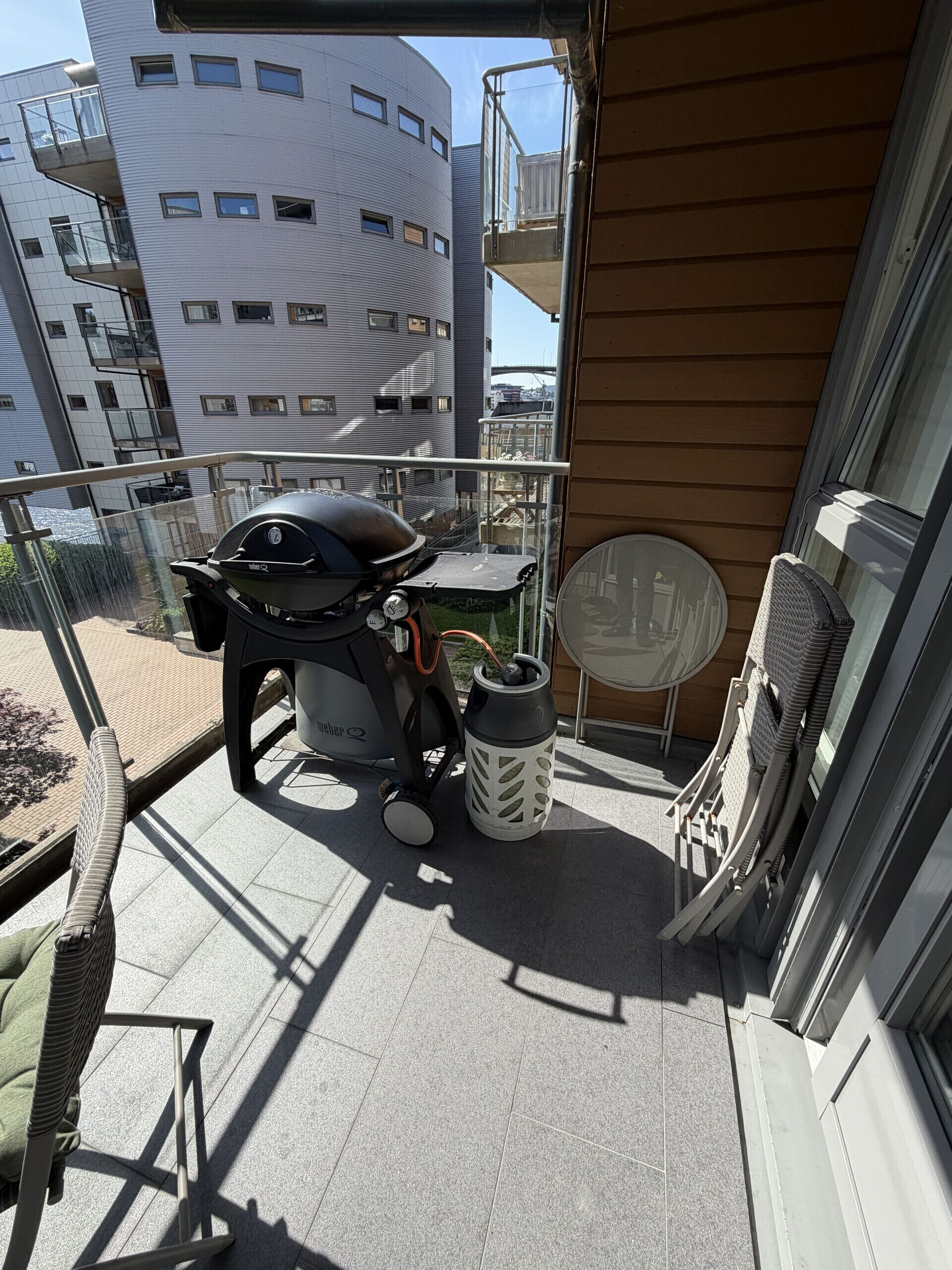 A balcony with a grill, a table, chairs, and a water bottle.