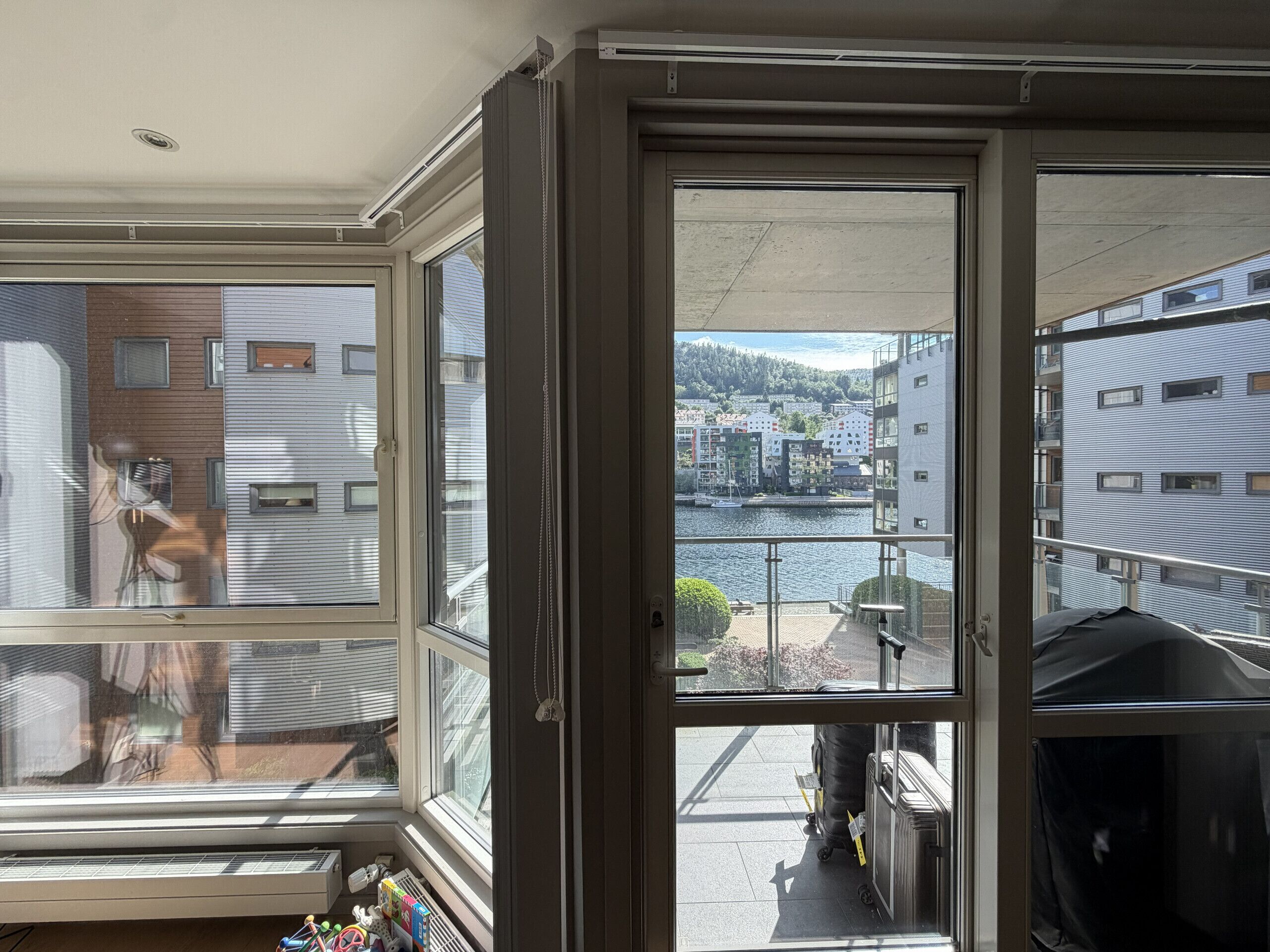 A room with a large window, a radiator, and a view of a body of water and buildings.