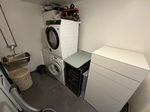A compact laundry room with a stacked washer and dryer, a small sink, and a trash bin. - Modern apartment Møhlenpris with seaview (Bergen)