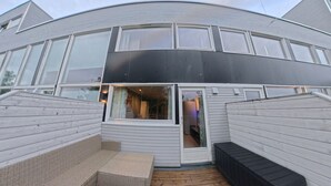 Ett modernt hus med en täckt uteplats, stora fönster och ett välvt tak.