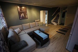 Ein modernes Wohnzimmer mit einem Ecksofa, einem Couchtisch, einem Schrank und einer Treppe, die in ein Obergeschoss führt.